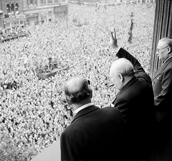 Churchill on balcony waving to crowds.
